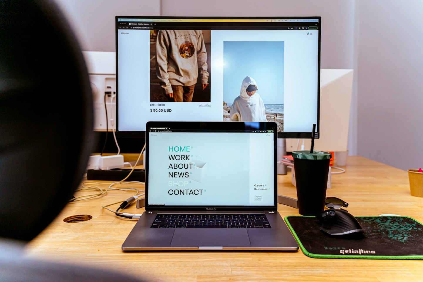 Orang bekerja di laptop dan monitor menampilkan situs web e-commerce.