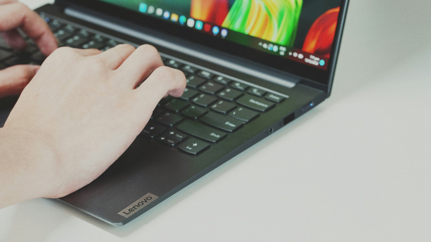 Tangan mengetik di keyboard laptop abu-abu gelap.